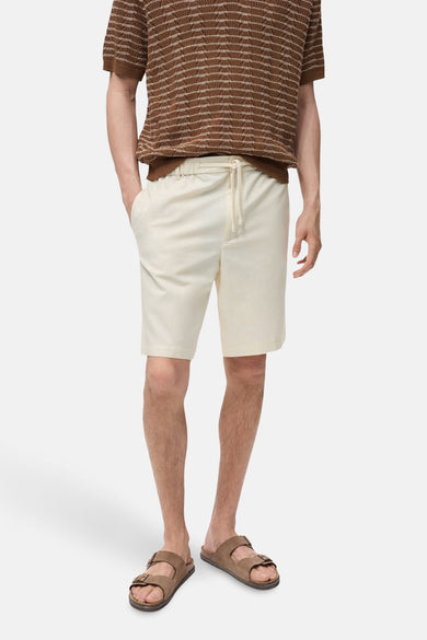Ecru short van MANGO, met een trekkoord in de taille en gedragen met bruine sandalen en een bruin gestreept shirt.
