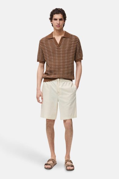 Ecru short van MANGO, met een elastische tailleband en een trekkoord, gecombineerd met een bruin gestreepte polo en sandalen.