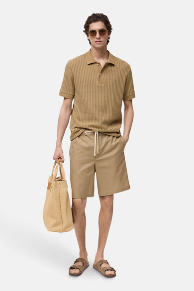 Beige short van MANGO, gecombineerd met een gebreide polo, bruine sandalen en een gevlochten tas.
