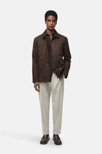 Grijze kostuumbroek van MANGO, gedragen met een bruin overhemd en jas, en donkerbruine loafers.
