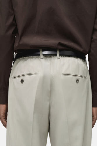 Grijze kostuumbroek van MANGO, achterkant gezien met zakken en bruine riem.