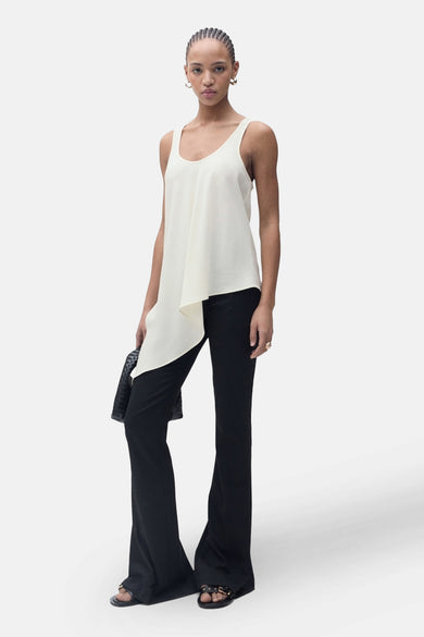 Ecru blouse zonder mouwen van MANGO, met asymmetrisch design en gedragen met zwarte, uitlopende broek en sandalen.
