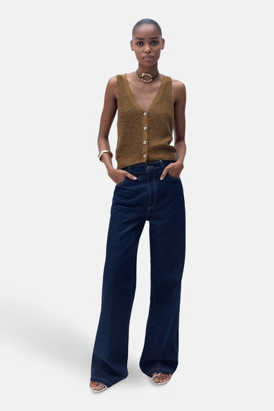 T-shirt marron de MANGO, avec fermeture à boutons devant, associé à des jeans larges bleu marine et un bracelet et une chaîne d'or.