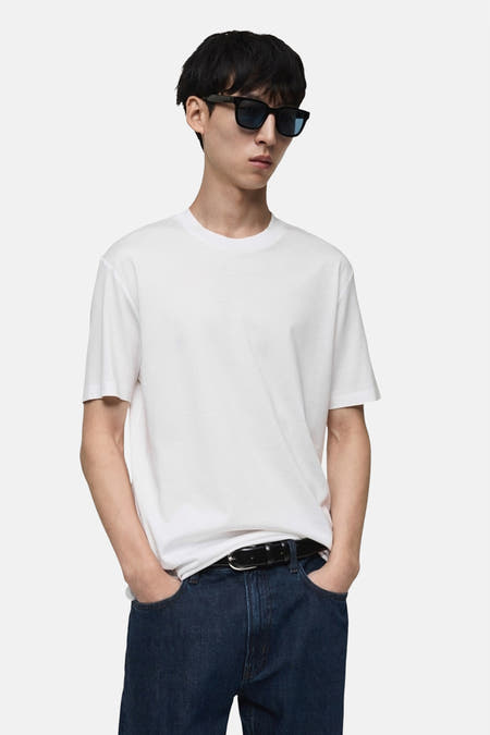 Wit T-shirt met korte mouwen van MANGO, gedragen met een donkerblauwe jeans en zwarte riem.