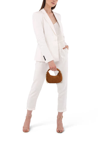 Beige suède-look handtas van Access® met goudkleurige studs en kettingdetails, gedragen door een model in wit pak.