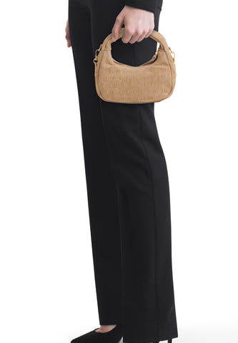 Beige suède handtas van Access® met gouden studs, gehouden door een persoon in zwarte kleding.