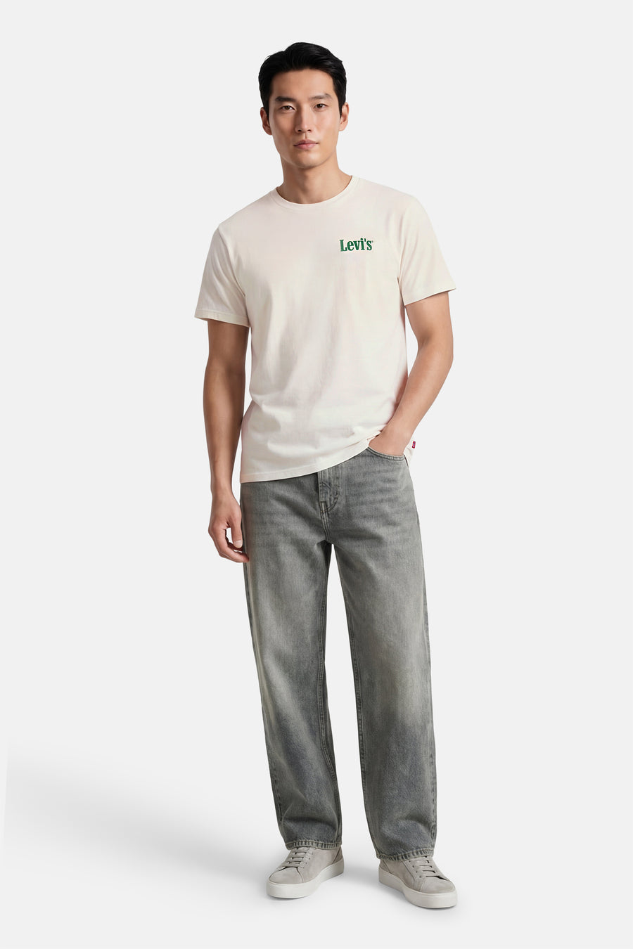 Beige T-shirt met korte mouwen van Levi's, met een groene logo op de borst, gedragen met grijze jeans en sneakers.
