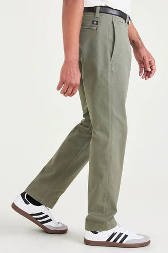 Groene chino van DOCKERS, met zwarte riem en witte sneakers met zwarte strepen in zij-aanzicht.
