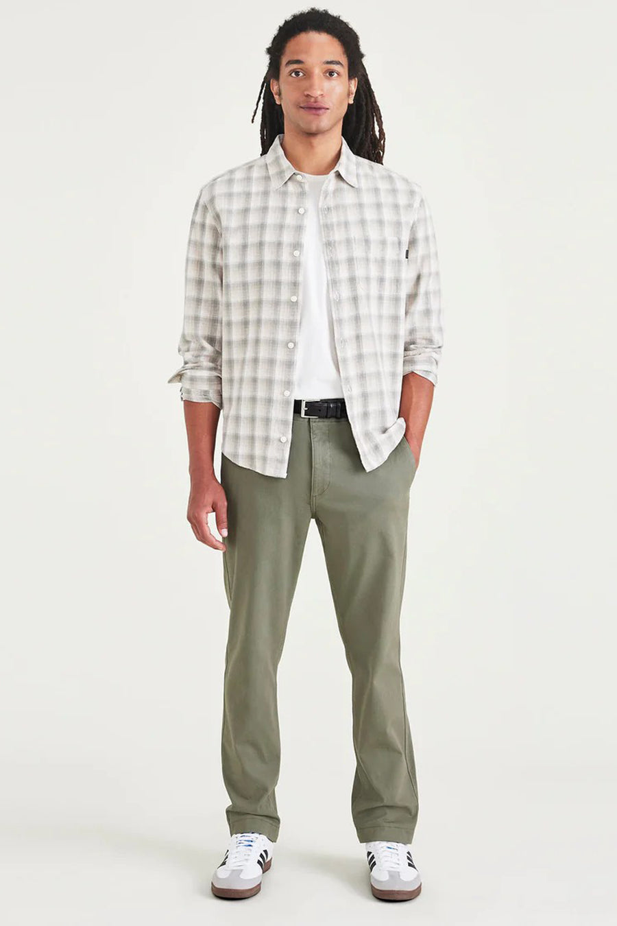 Man in geruit overhemd, groene broek en witte sneakers.