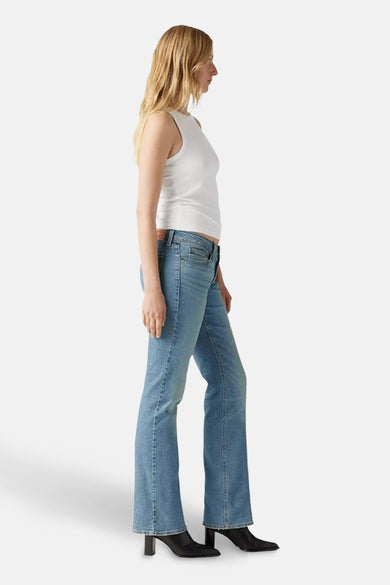 Lichtblauwe bootcut jeans van Levi's, gedragen met een wit hemd en zwarte laarzen met hak, in zijaanzicht.