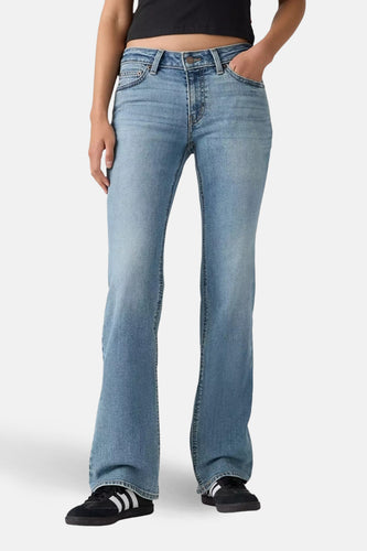 Bootcut jeans van midblauw denim van Levi's, gecombineerd met zwarte schoenen met witte strepen.
