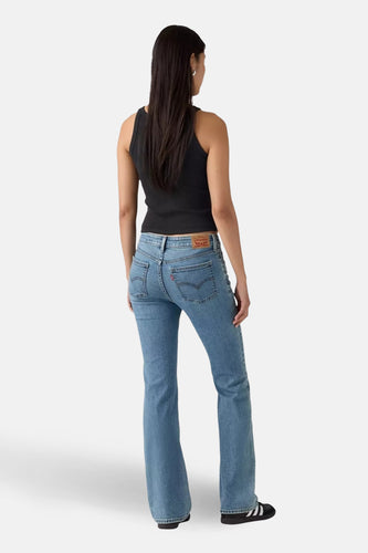 Bootcut jeans van blauw denim van Levi's, gezien van achteren, gecombineerd met een zwarte top en zwarte schoenen met strepen.
