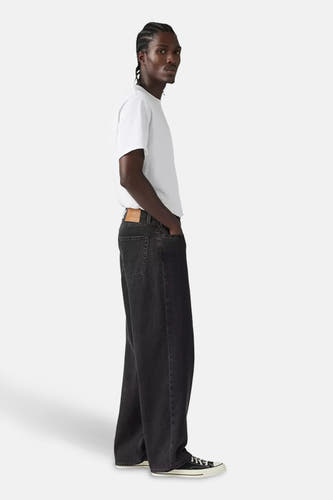 Wijde donkergrijze jeans van Levi's, gedragen met een wit T-shirt en zwarte sneakers, zij-aanzicht.
