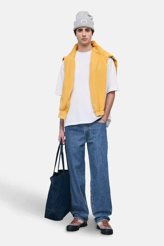 Wijde jeans van blauw denim van Levi's, met een witte T-shirt, gele trui en een grijze muts.
