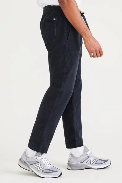 Blauwe broek van DOCKERS, met trekkoord en grijze New Balance sneakers, in een zij-aanzicht.
