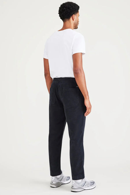 Blauwe broek van DOCKERS, gezien van achteren, met een wit t-shirt en grijze sportschoenen.
