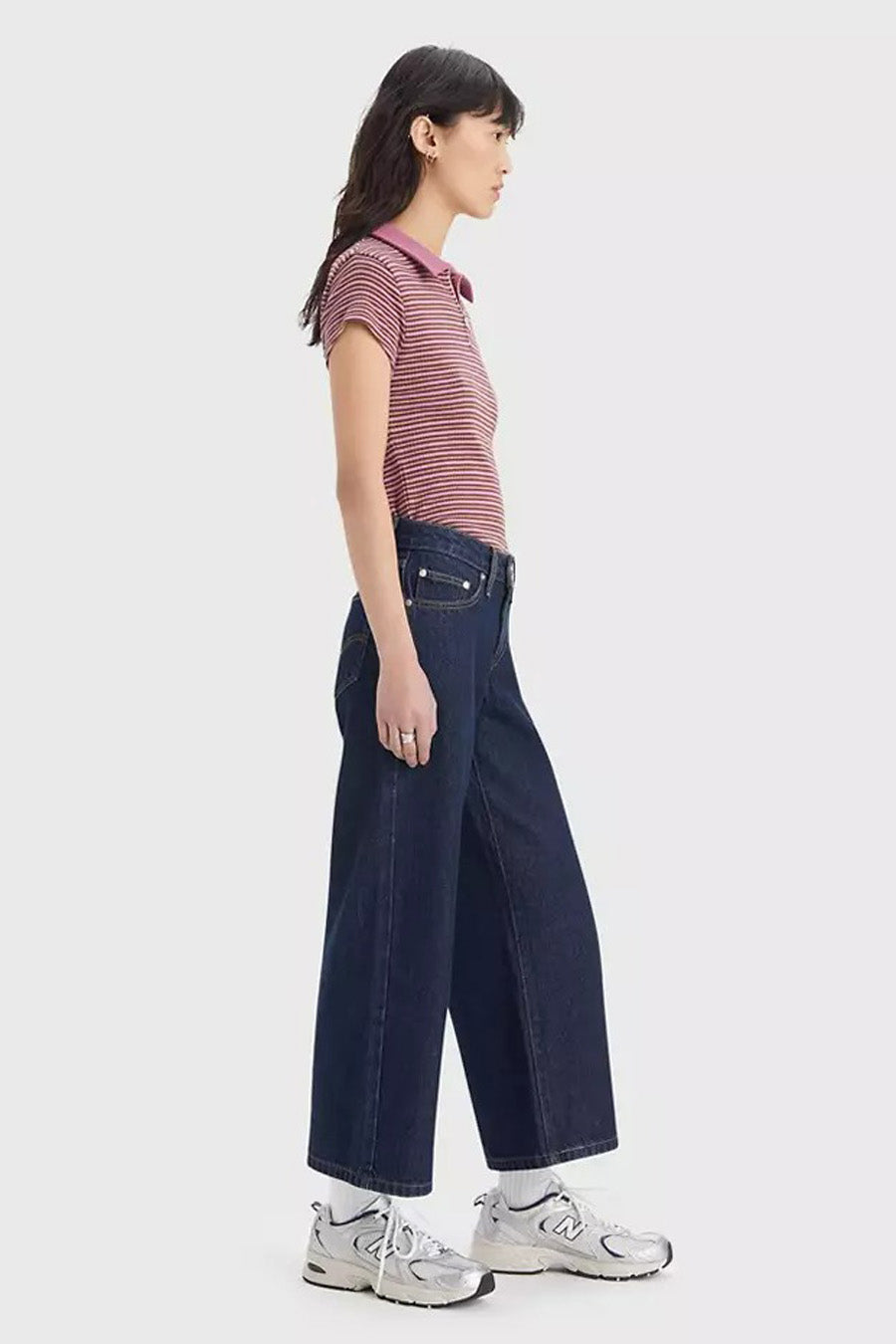 Donkere blauwe wijde jeans van Levi's, met een donkere wassing, gecombineerd met een gestreepte top en witte sneakers.