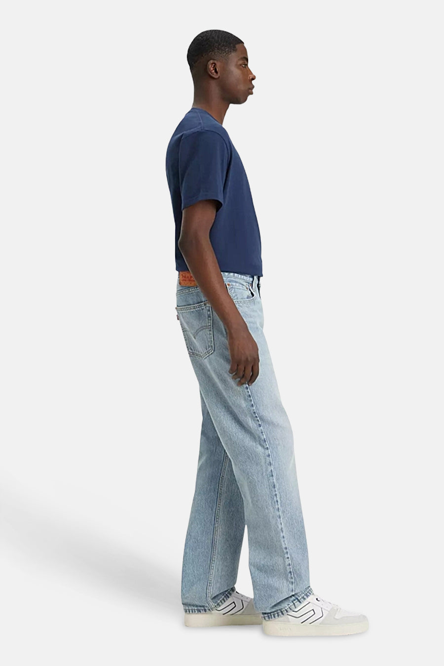 Jean en denim bleu clair droit de Levi's, montré en vue latérale, associé à un t-shirt bleu foncé et des baskets blanches.