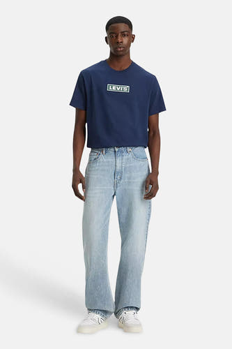 Jean droit bleu clair de Levi's, associé à un t-shirt bleu foncé avec logo et des baskets blanches.