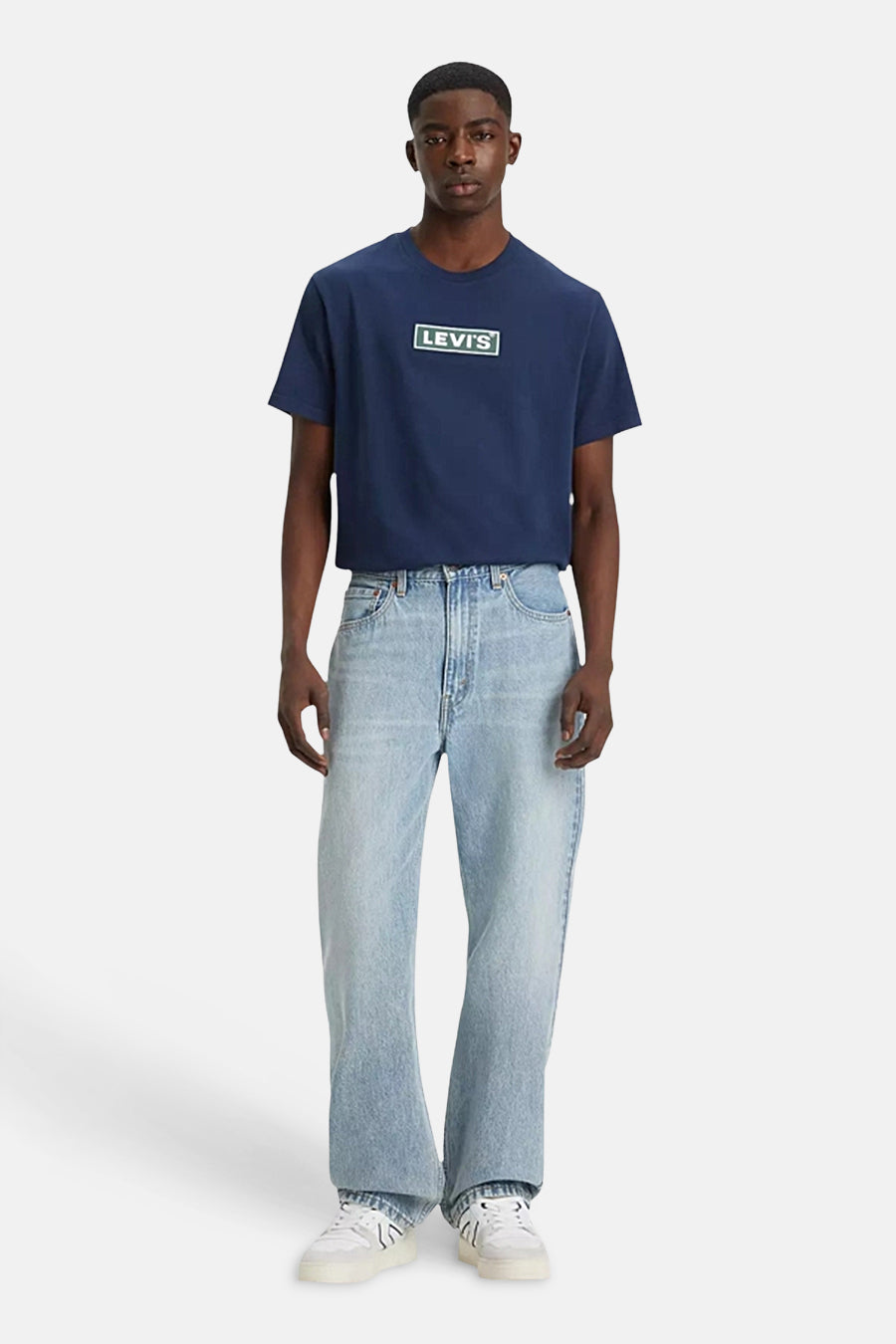 Jean droit bleu clair de Levi's, associé à un t-shirt bleu foncé avec logo et des baskets blanches.