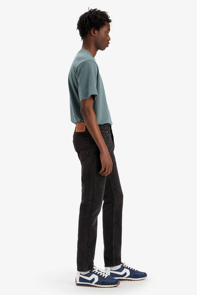 Jean droit de denim gris foncé de Levi's, regardé sur le côté, associé à un T-shirt bleu-vert et des baskets bleues.