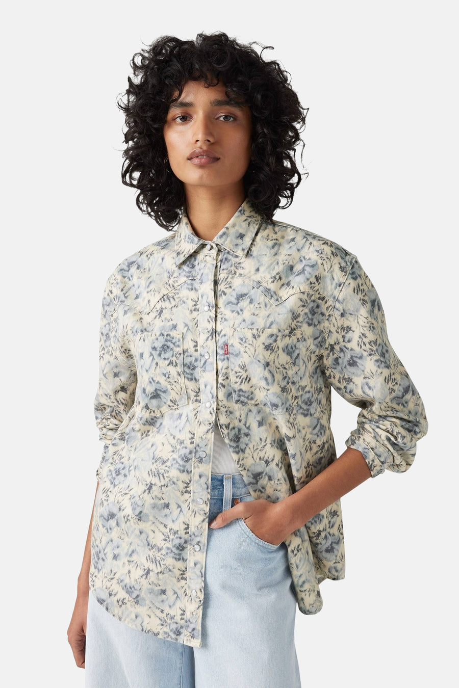 Blauw jeanshemd van Levi's, met lange mouwen, bloemenpatroon en rode merklabel, gecombineerd met een lichtblauwe jeans.

