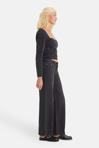 Jean wide bleu foncé de LEVI'S YOUTH, avec un modèle portant une chemise noire et des chaussures, en vue de dos.
