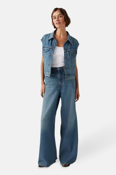 Jean droit en denim bleu moyen de Levi's, associé à un haut blanc et un gilet en denim.