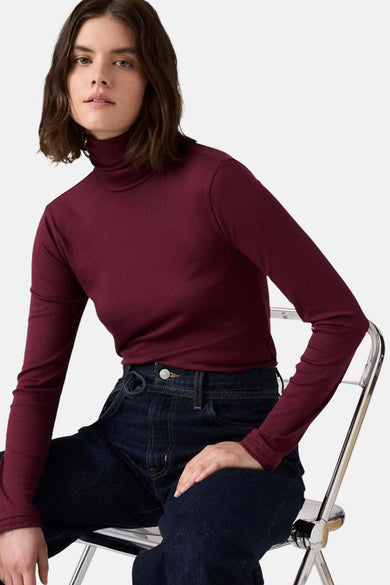 Bordeaux T-shirt met lange mouwen van Levi's, gedragen met donkere jeans en zilveren stoel op witte achtergrond.
