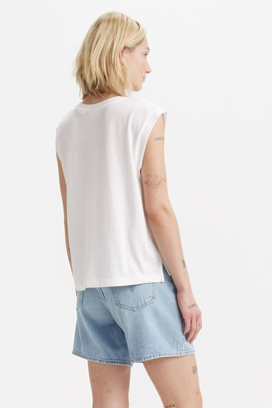 Witte top zonder mouwen van Levi's, met korte, blonde haren en spijkerbroek.