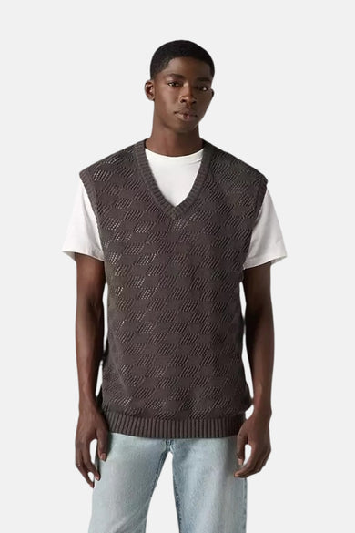 Man in een grijze gebreide trui vest met een witte t-shirt en lichte jeans.