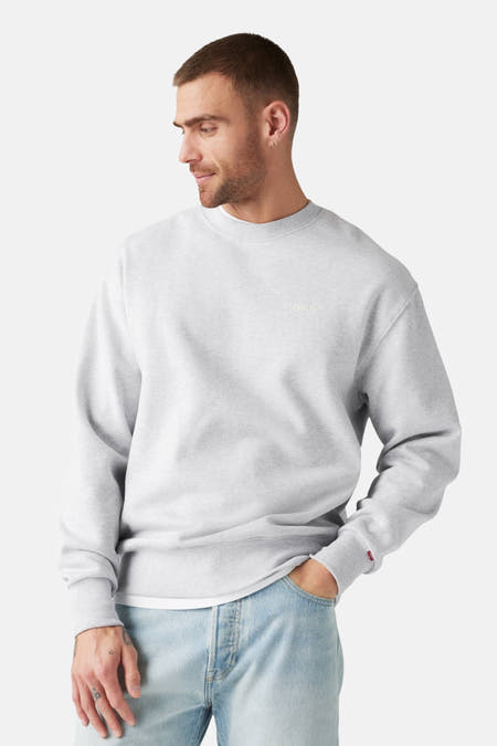 Grijze sweater met ronde hals van Levi's, met kleine rode merklabel op de mouw en denim broek.
