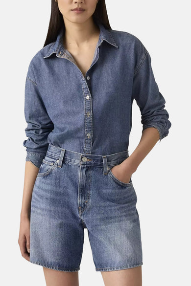 Short en jean bleu de Levi's®, porté au dos par une femme avec une chemise en jean et des mocassins noirs.