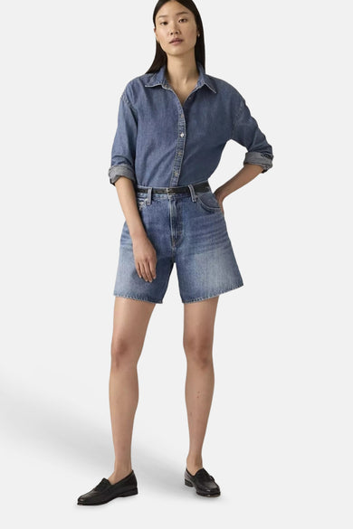 Short en jean bleu moyen Levi's® à jambes larges, porté avec une chemise en jean, une ceinture noire fine et des mocassins.