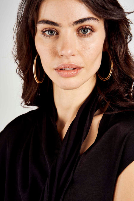 Zwarte blouse met drapering en korte mouwen van Astrid Black Label, close-up op model met gouden oorbellen