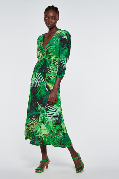 Groen kleedje met tropisch bladpatroon van Astrid Black Label, lange mouwen, V-hals en waaierrok, model in volledige lengte.