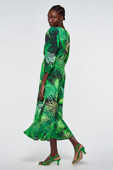 Groen kleedje met tropisch bladpatroon van Astrid Black Label, lange mouwen, zijden textuur, model in zijaanzicht met groene hakken