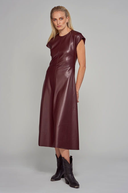 Mouloze bordeaux kleurige jurk van Astrid Black Label, met een gladde lederlook en gecombineerd met zwarte laarzen.

