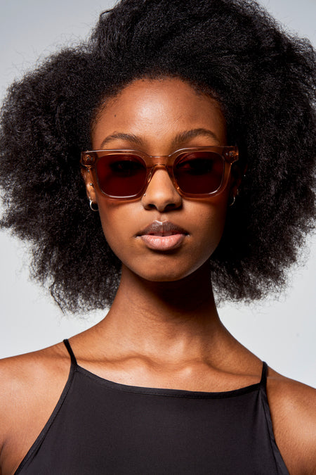Lunettes de soleil taupe d'Astrid Black Label, portées par un modèle avec un haut noir et des cheveux relevés.