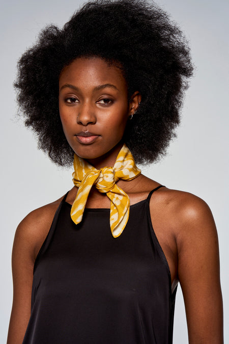 Gele zomersjaal van Astrid Black Label, geknoopt rond de hals, gedragen met een zwarte top.
