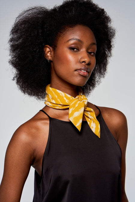 Gele zomersjaal van Astrid Black Label, geknoopt gedragen, met een wit gestreept patroon en een zwarte top.
