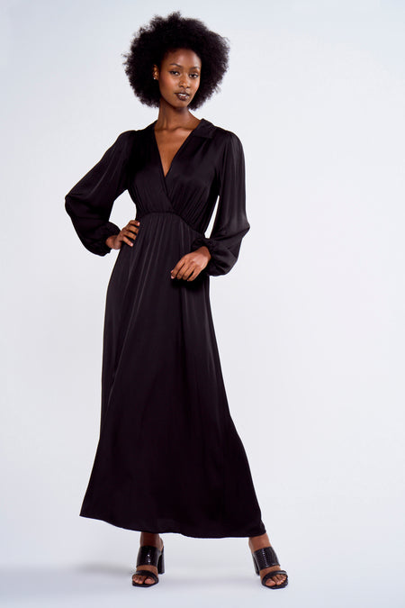 Robe noire à longues manches d'Astrid Black Label, avec une jupe évasée et portée avec des sandales noires à talon.