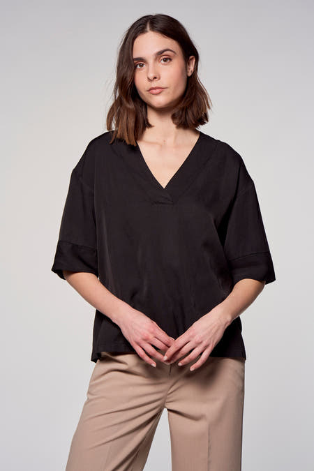 Zwarte blouse met korte mouwen van Astrid Black Label, effen stof met v-hals en beige pantalon.
