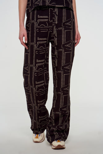 Zwarte broek van Astrid Black Label met een beige letterpatroon en bijpassende sneakers.
