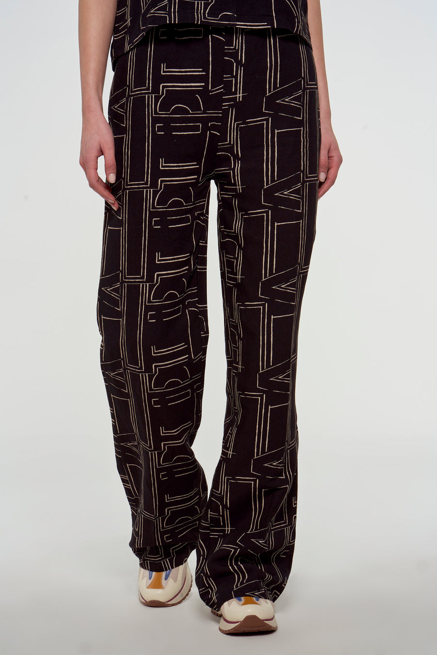 Zwarte broek van Astrid Black Label met een beige letterpatroon en bijpassende sneakers.

