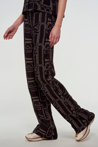 Zwarte broek met geometrisch patroon van Astrid Black Label, gecombineerd met crèmekleurige sneakers, in een zijdelings shot.
