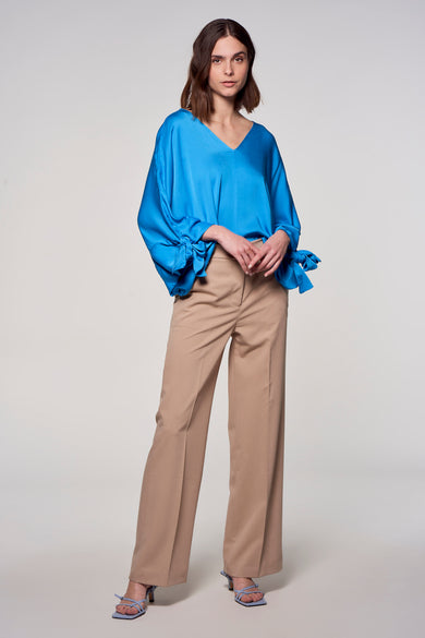 Blauwe blouse van Astrid Black Label, met lange mouwen en strikdetails, gecombineerd met kaki pantalon en blauwe hakken.
