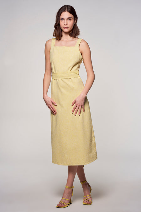 Gele mouwloze jurk van Astrid Black Label, met een ceintuur en gedragen met gele hakken.
