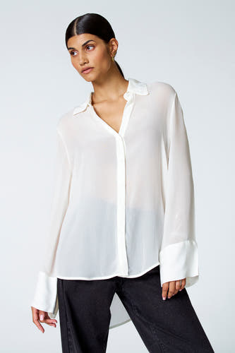Ecru blouse met lange mouwen van Astrid Black Label, met manchetten en gedragen met een donkere broek.
