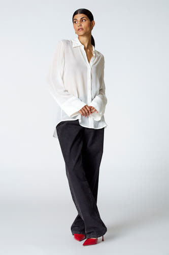 Ecru blouse met lange mouwen van Astrid Black Label, gecombineerd met zwarte broek en rode pumps.
